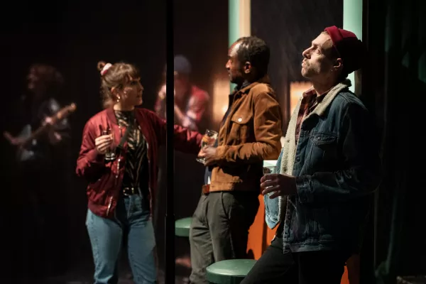 Visuel du spectacle Sans suite un air de roman, les comédiens boivent un verre dans la rue pendant qu'il y a un concert derrière eux