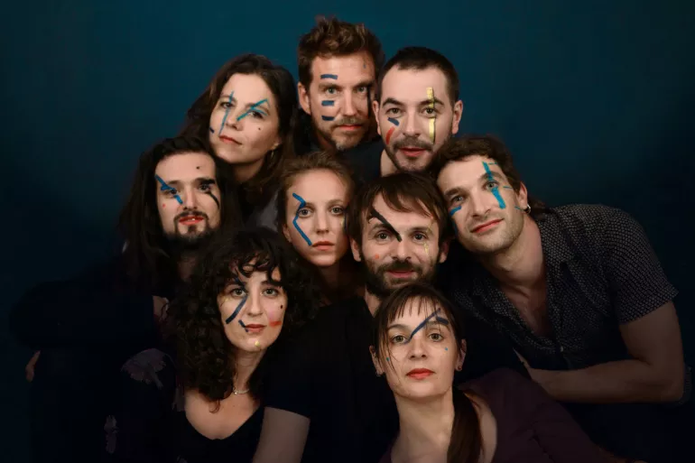 Neuf visages cinq visages d’hommes et quatre visages de femmes forment un cercle plein. Sur leurs visages au niveau des yeux, des joues et même du front, se trouvent des traits et des points de peintures aléatoires. Majoritairement il s’agit de peintures colorées fluorescentes qui réagissent à la lumière. Leurs expressions sont neutres mais quelques-uns sourient légèrement. 