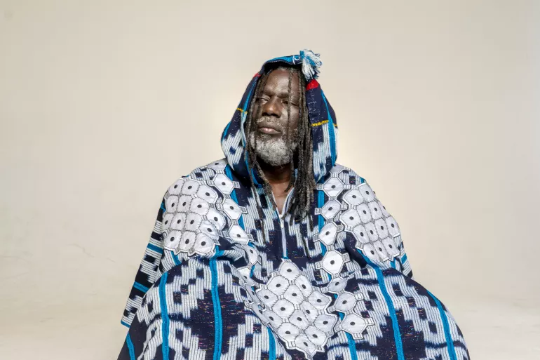 Devant un fond blanc, le chanteur Tiken Jah Fakoly est assis par terre. Il est habillé d’un poncho décoré de motifs aléatoires dans un style traditionnel africain. Les tons sont majoritairement bleus et blancs mais quelques détails rouges et jaunes parsèment sa tenue. La capuche qui recouvre sa tête laisse voir ses dreadlocks et son visage. Il a les yeux entrouverts et regarde sur le côté gauche. Le vêtement recouvre entièrement son corps. 